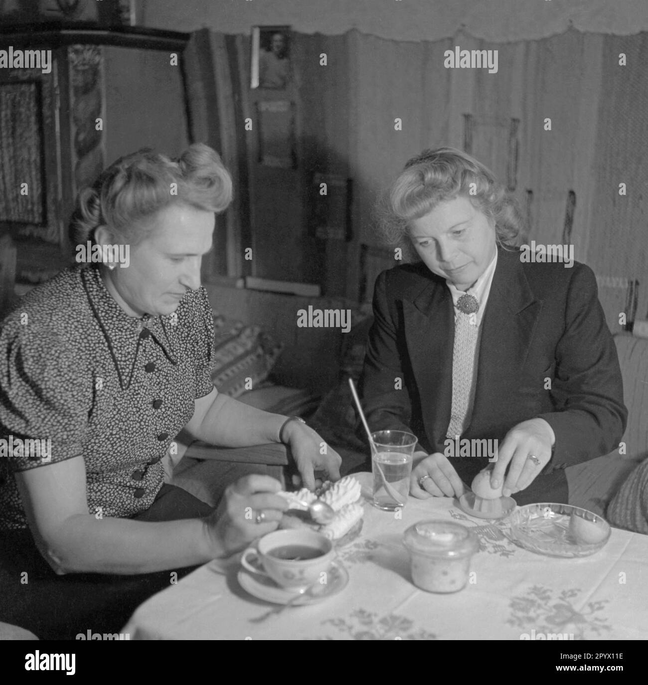 Zwei Frauen sitzen zusammen an einem Tisch, eine presst eine Zitrone aus. Stockfoto