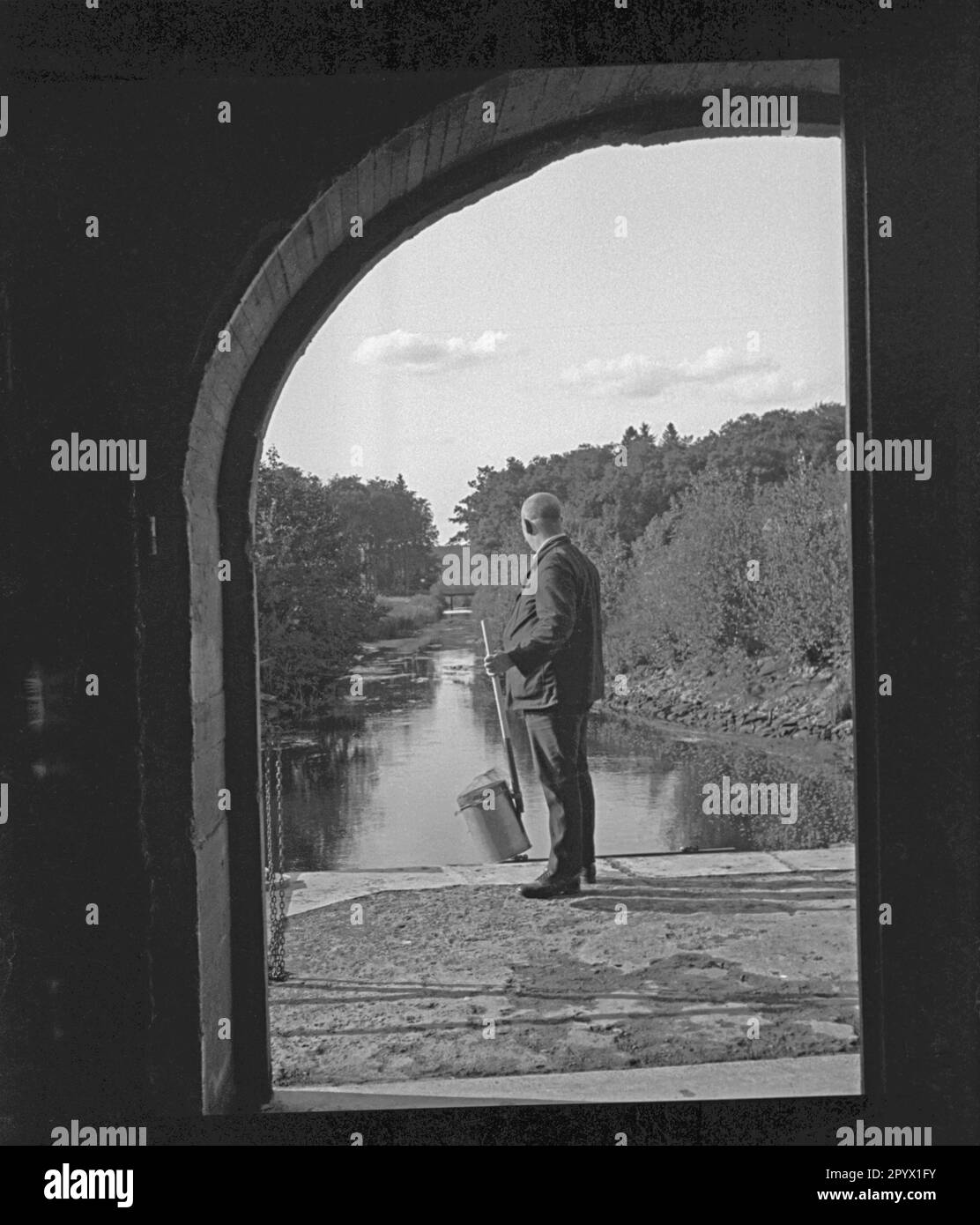 Ein Mann mit Landenetz sieht in die Entfernung eines Mühlenteichs. Stockfoto