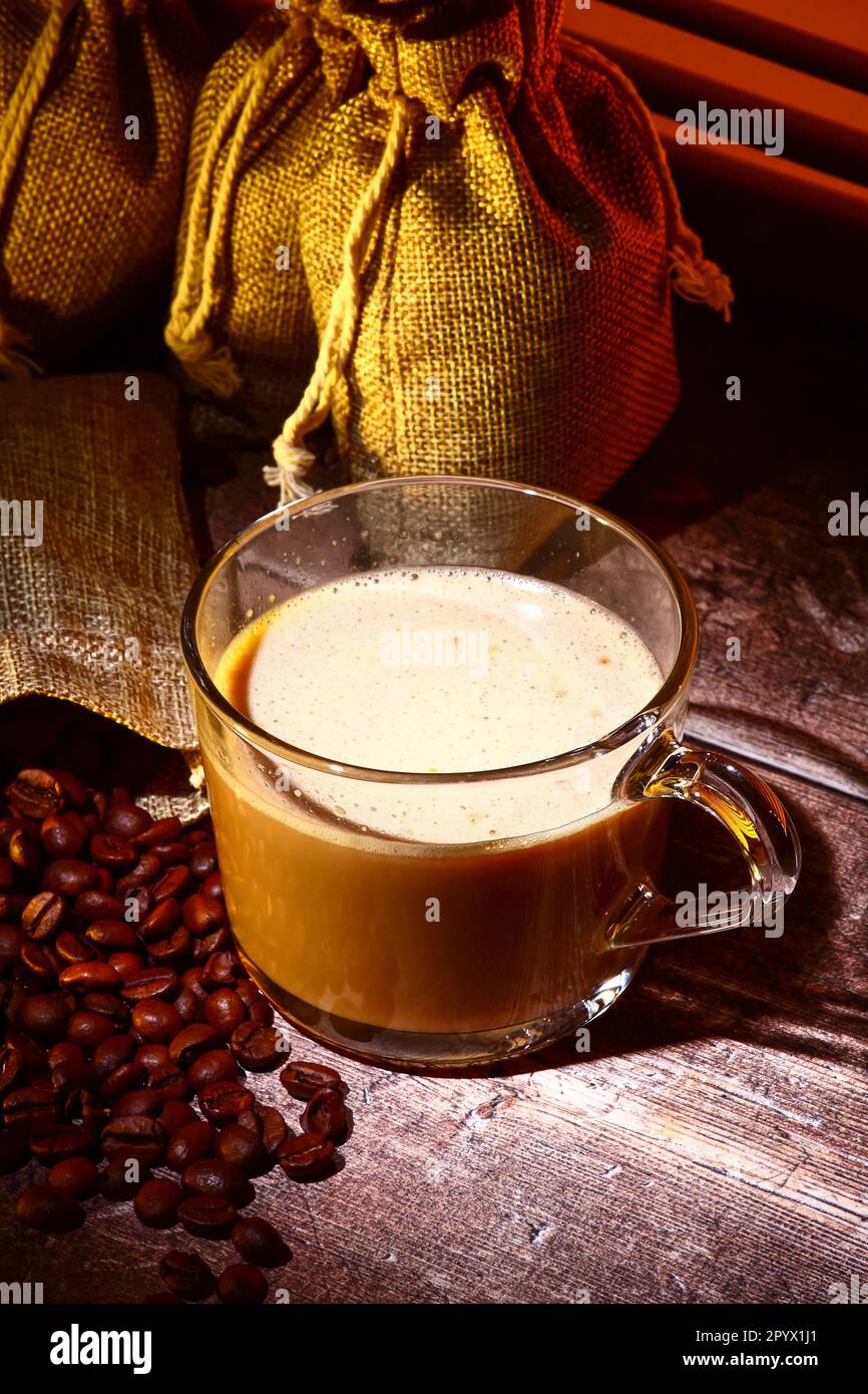 Glas-Kaffeetasse mit Säcken roher gerösteter Kaffeebohnen Stockfoto