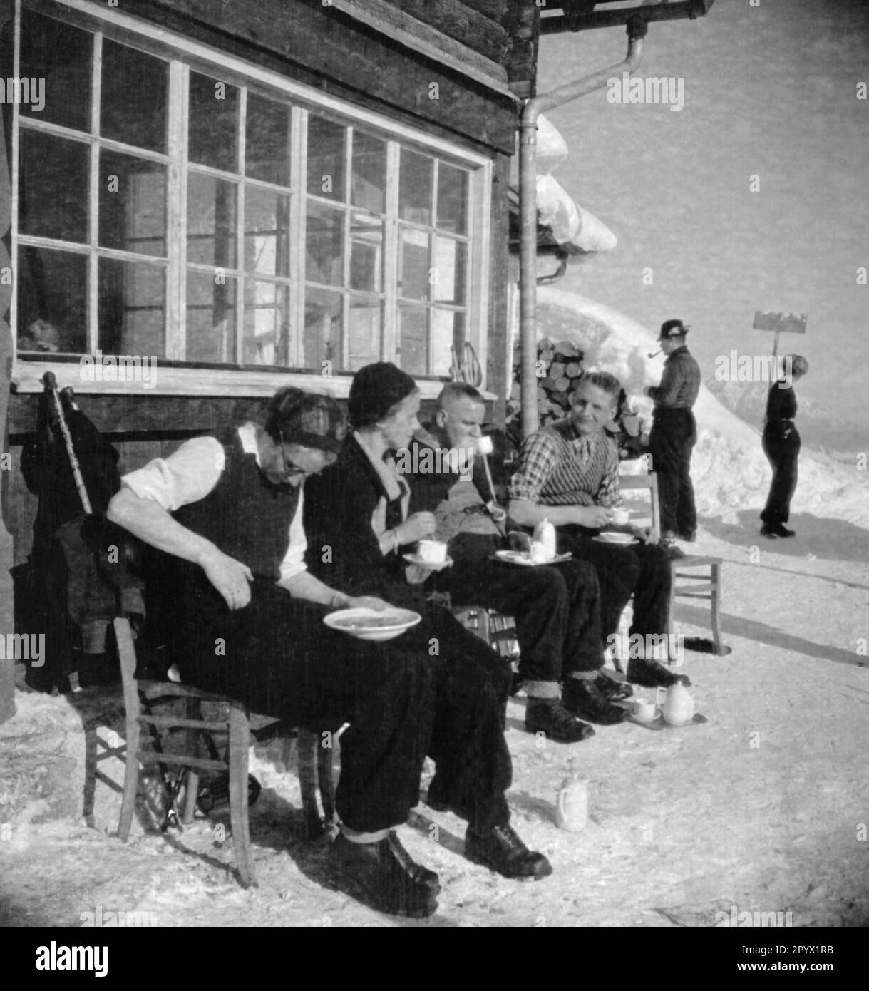 Auf der Bank vor einer Hütte genießen die Sportler die Sonne und die warmen Getränke. Unbefriedigtes Bild, wahrscheinlich im Winter 1933/34 Stockfoto