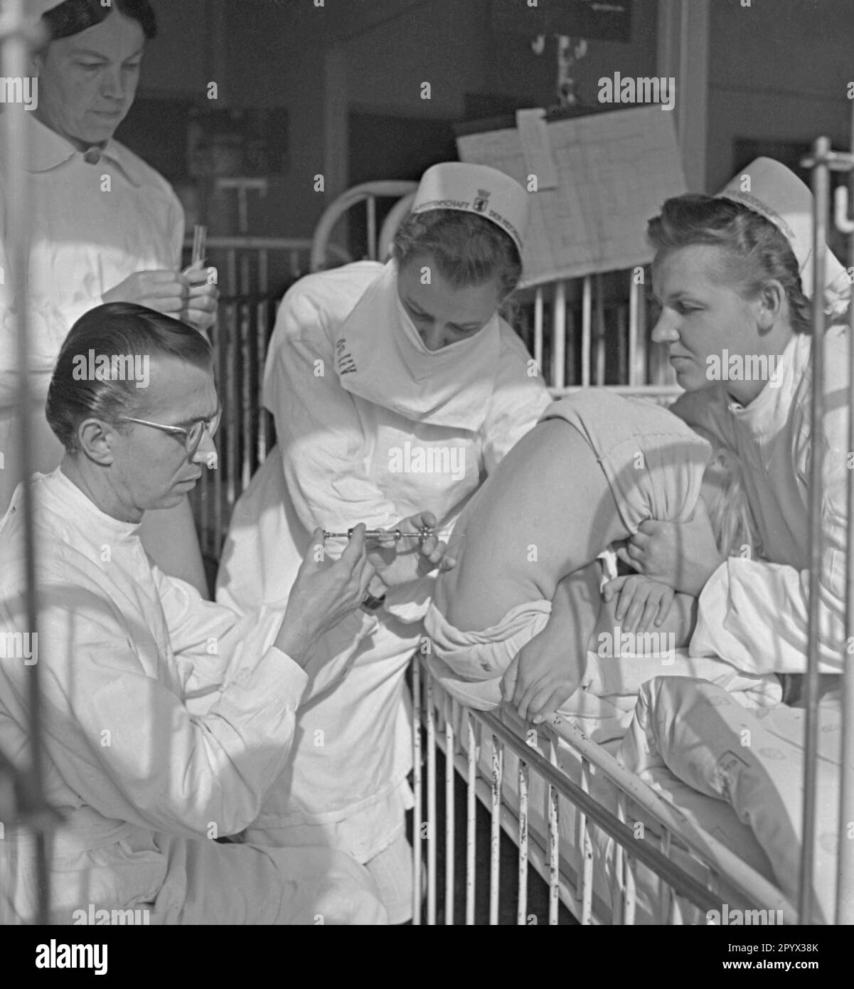 Ein Arzt injiziert einem Patienten, der von einer Krankenschwester gehalten wird, ein Medikament in den Rücken. Stockfoto