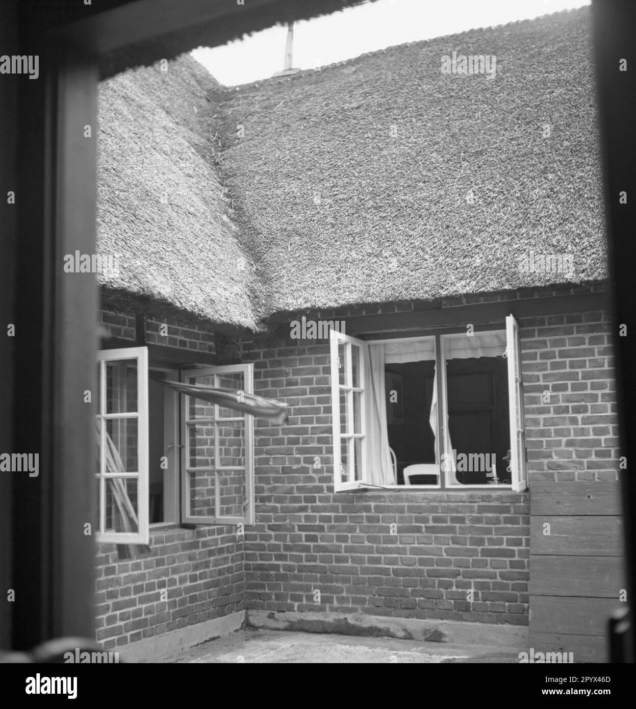 Undatiertes Foto des Innenhofs eines strohgedeckten Hauses in der Nähe von Husum, Nordfriesland, Schleswig-Holstein um 1940. Die Fenster werden zur Luft geöffnet. Die Vorhänge flattern im Wind. Stockfoto