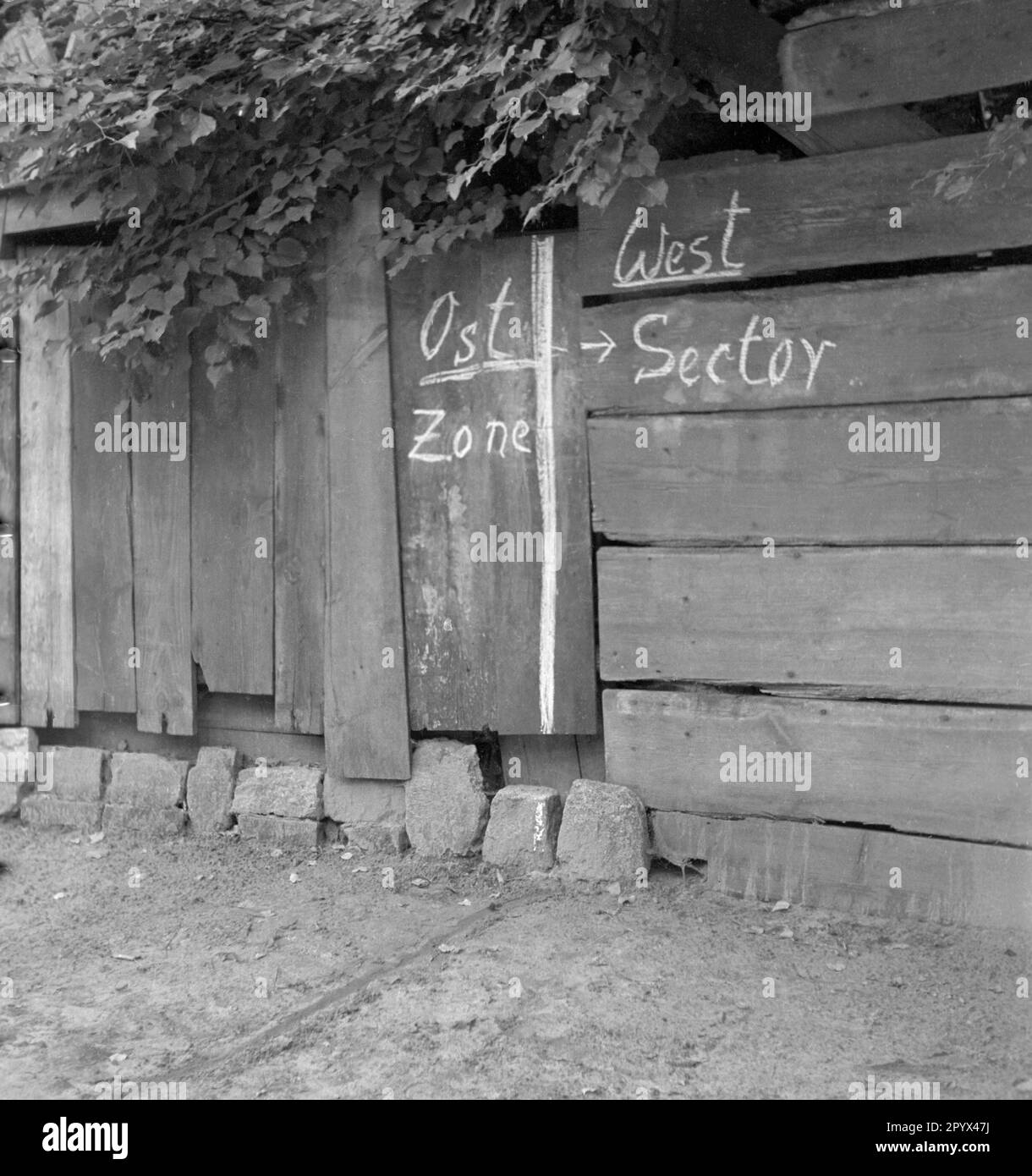 Foto eines Kreidezeichens der Zonengrenze zwischen West- und Ostteil Berlins im Jahre 1950. Auf dem Boden wird die Markierung durch eine im Sand gezogene Linie fortgesetzt. Das Foto wurde nach der Währungsreform 1948 in einem Restaurant für Tagesausflüge aufgenommen, das direkt an der Zonengrenze zwischen Ost- und Westberlin lag. Stockfoto