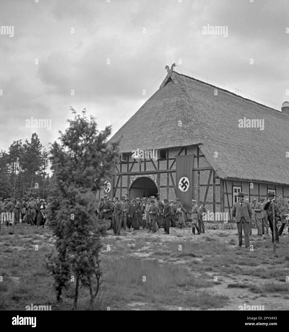 Foto des Landtagsplatzes am Landtagsplatz in Hoesseringen in Sudeburg in der Heide Lueneburg anlässlich seiner Eröffnung am 28. Juni 1936. Am Eingang des Bauernhauses (Niederdeutsches Reihenhaus mit Strohdach und Giebelverzierung, Pferdeköpfe) haben sich lokale Bauernvertreter (einige in SA-Uniformen) und Zuschauer versammelt. Hakenkreuz-Flaggen hängen am Gabel. Stockfoto