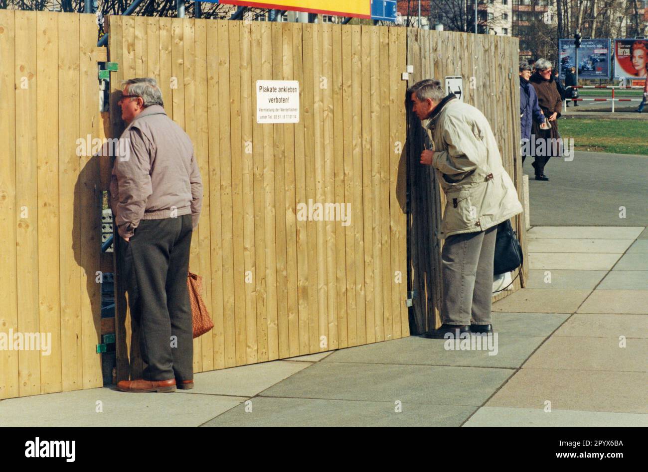 Neugierige Männer sehen mit einem Beobachtungsschlitz auf einer großen Baustelle auf Wiener Platzt in Dresden aus. Stockfoto