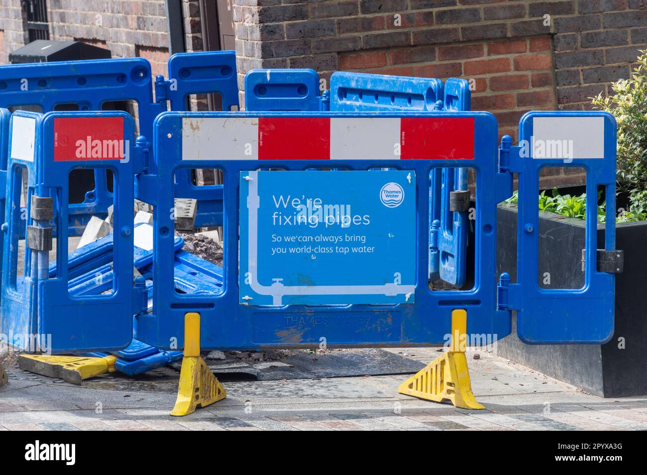 Thames Water Company blaue Barrieren in der Straße um das große Loch mit Schild mit der Aufschrift „We're fixed pipes“, Surrey, England, Großbritannien Stockfoto