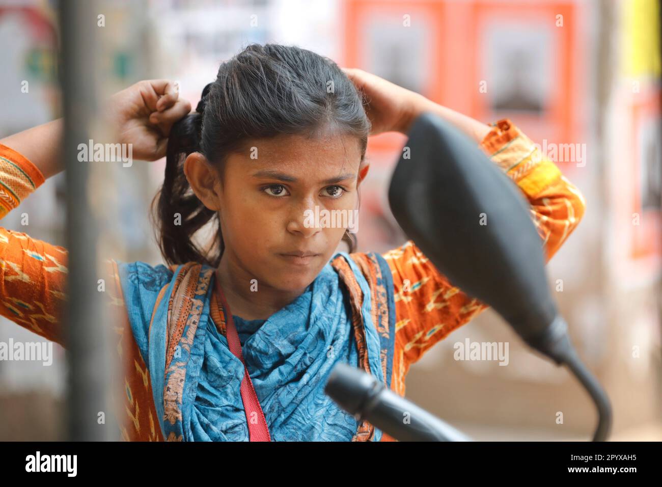 Dhaka, Bangladesch - 18. April 2023: Ein Straßenkind verkleidet sich im Dhaka-Universitätsviertel in B vor dem Spiegel eines Motorrads Stockfoto