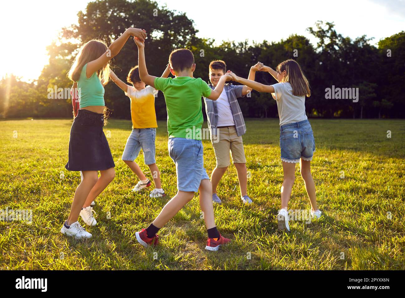 Gruppe glücklicher Kinder, die im Kreis tanzen, während sie im Sommer im Park gemeinsam spielen Stockfoto