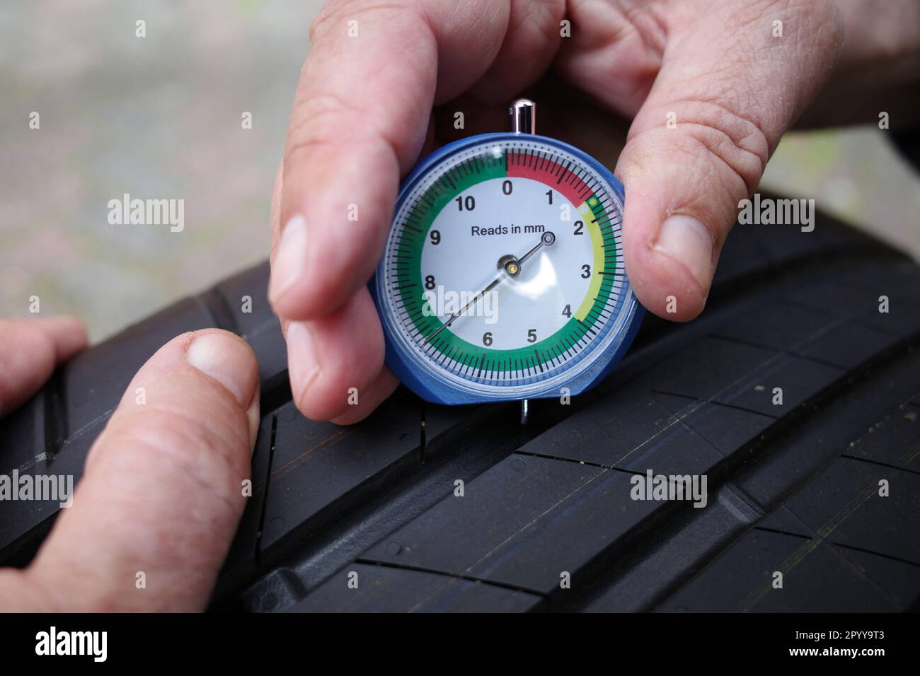 Die Hände eines Mannes messen die Profiltiefe eines Autoreifens in mm. Er drückt ein Messgerät in ein Reifenprofil, um dessen Tiefe zu messen. Die richtige Tiefe in t Stockfoto