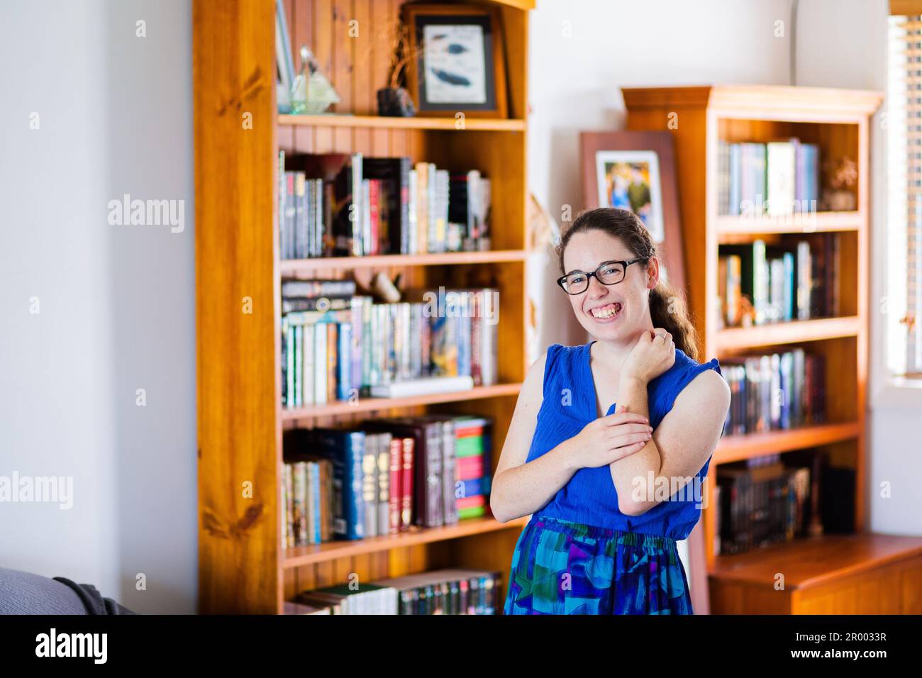 Porträt einer lächelnden jungen Frau in ihrem Haus mit Bücherregalen an Wänden voller fiktiver Geschichten Stockfoto