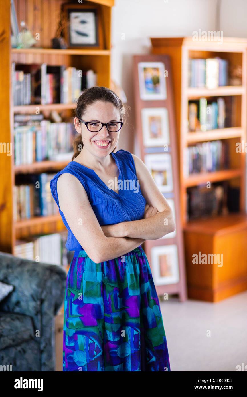 Porträt einer lächelnden jungen Frau in ihrem Haus mit Bücherregalen an Wänden voller fiktiver Geschichten Stockfoto