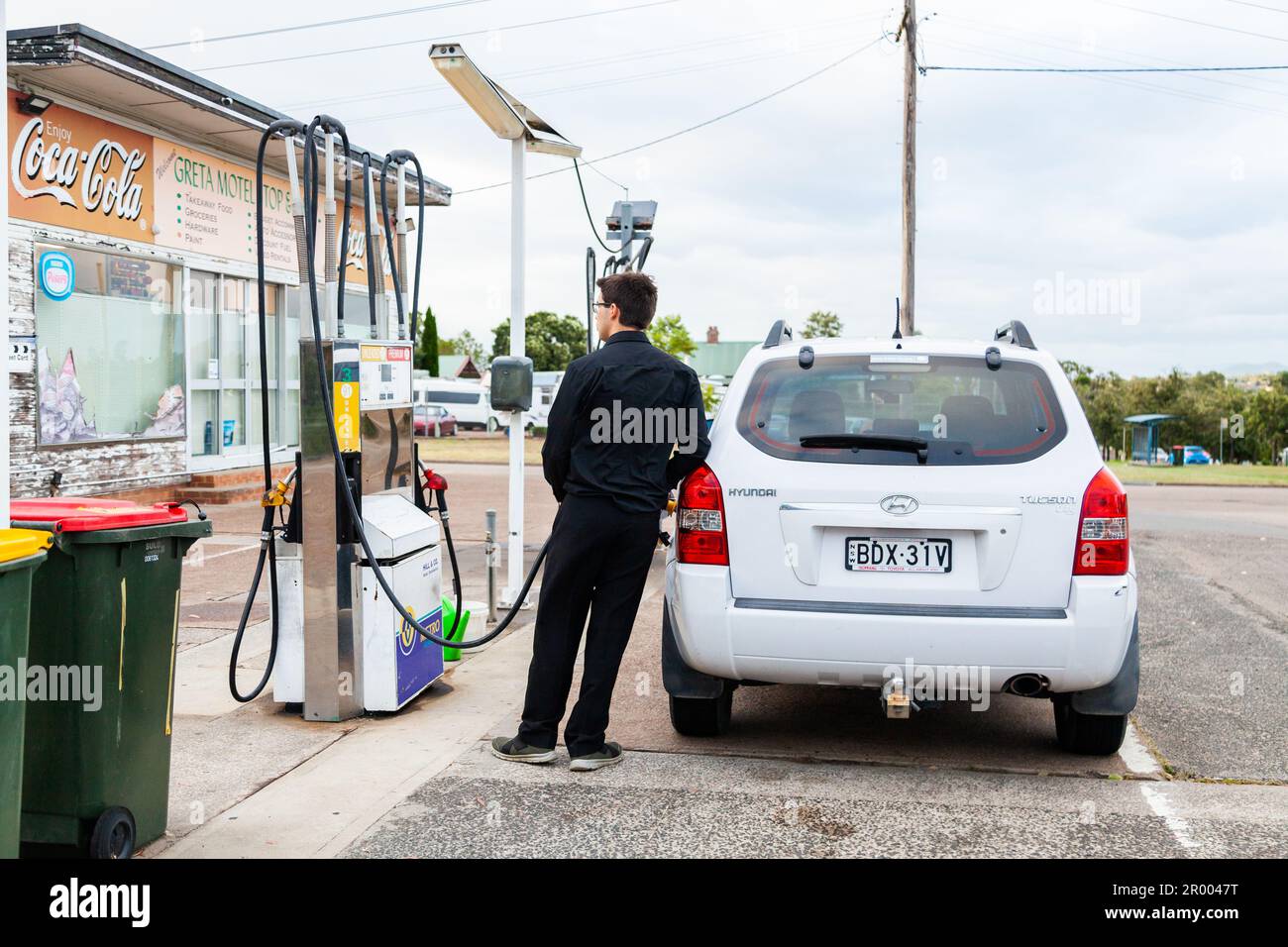Ein junger Mann in Schwarz betankt sein Auto an einer ländlichen Tankstelle in einer australischen Landstadt Stockfoto