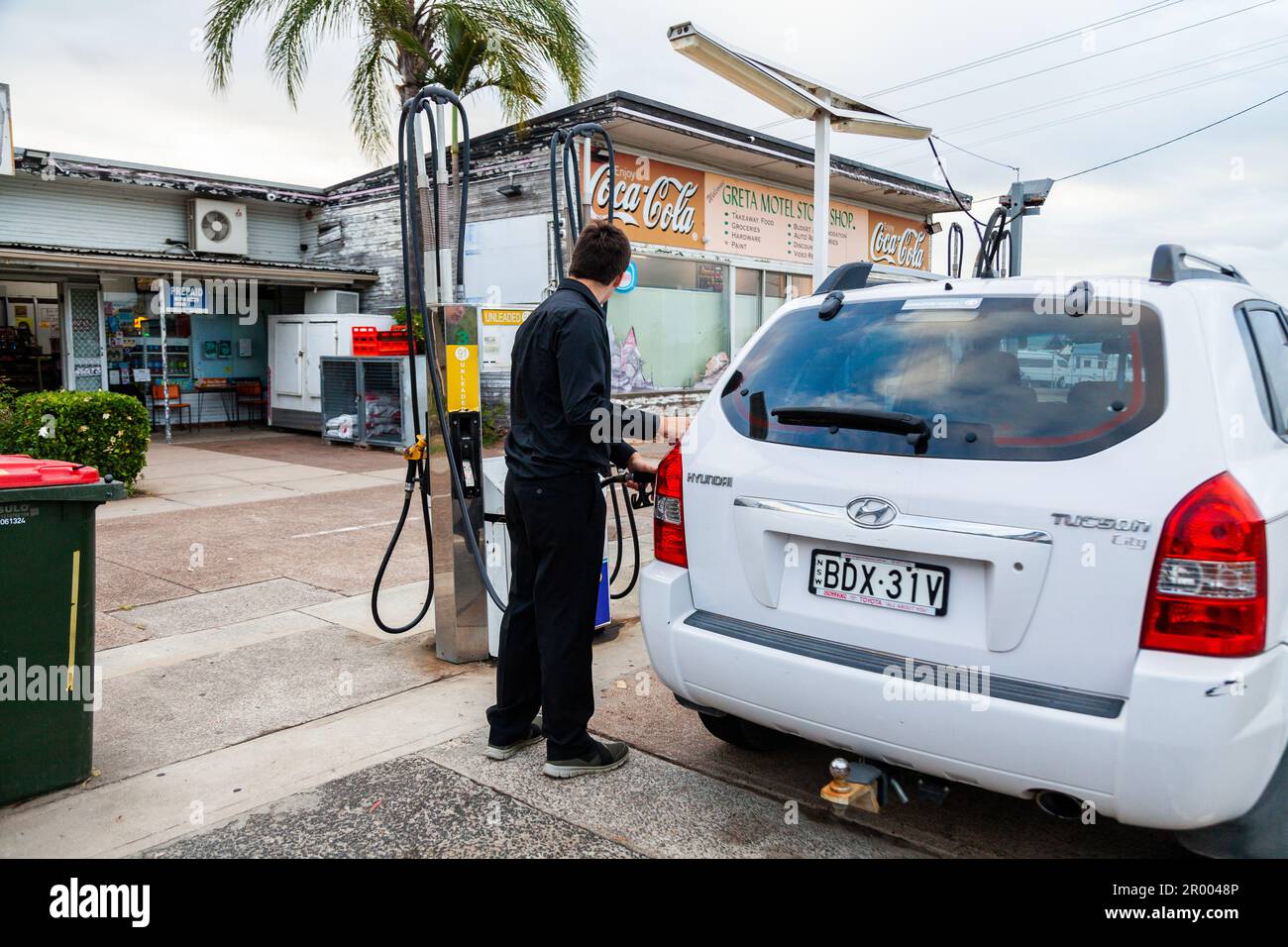 Ein junger Mann in Schwarz betankt sein Auto an einer ländlichen Tankstelle in einer australischen Landstadt Stockfoto