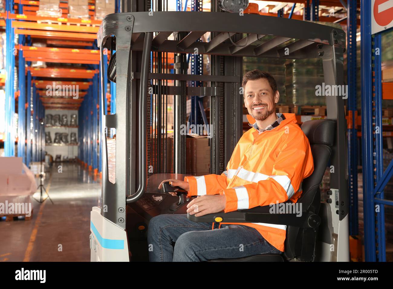 Glücklicher Arbeiter, der im Gabelstapler im Lager sitzt Stockfoto