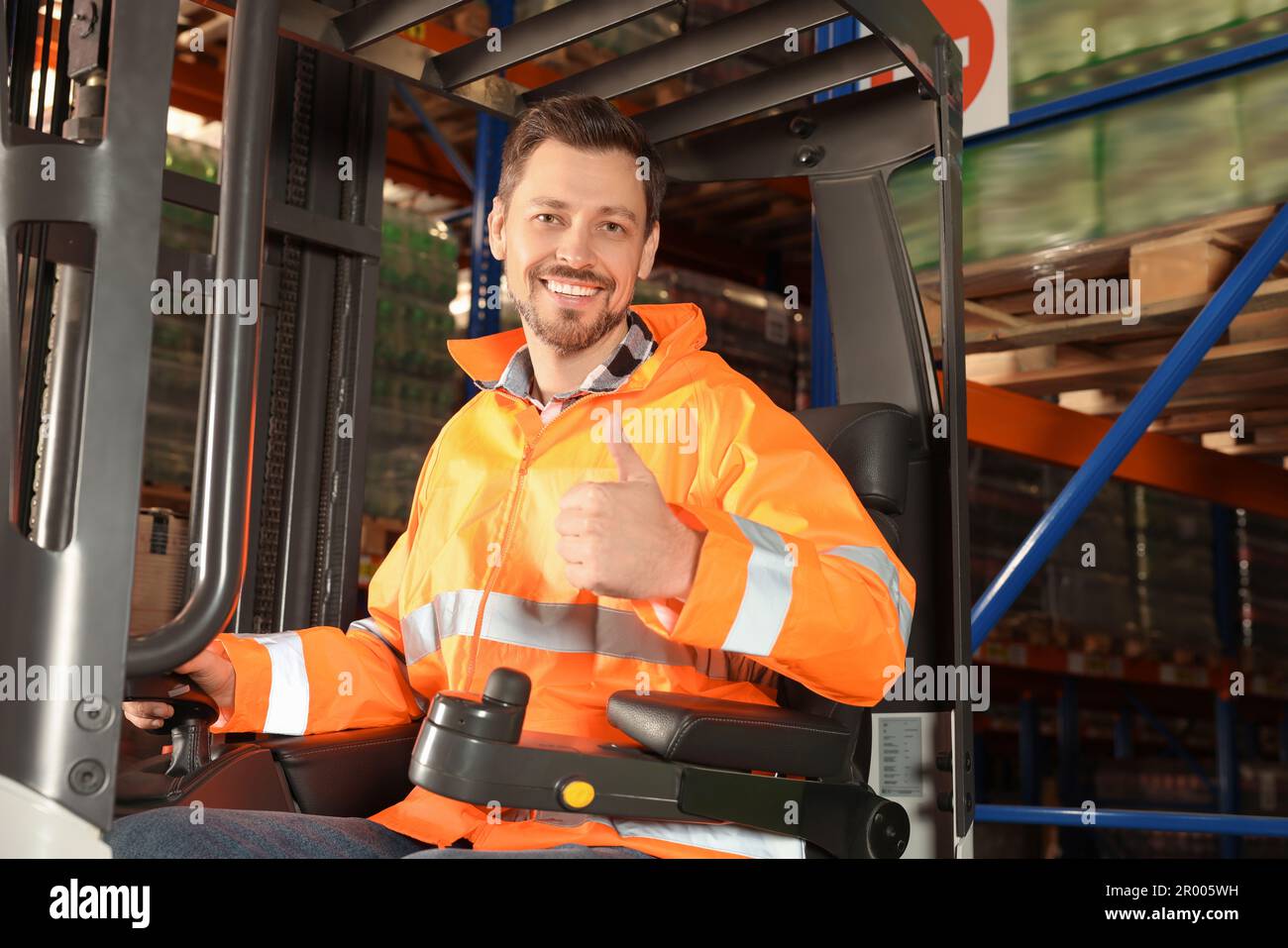 Glücklicher Arbeiter, der im Gabelstapler im Lager sitzt Stockfoto