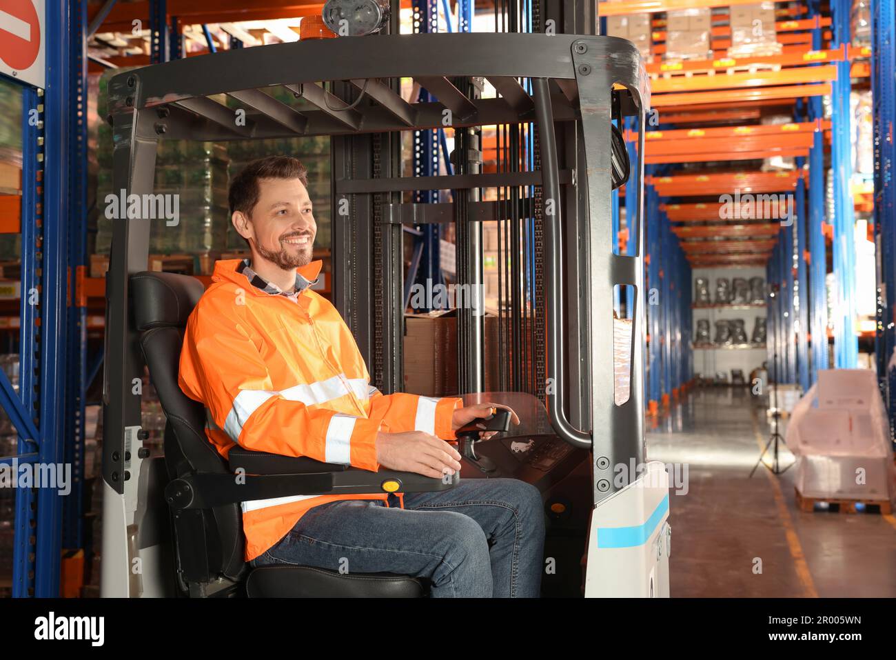 Glücklicher Arbeiter, der im Gabelstapler im Lager sitzt Stockfoto