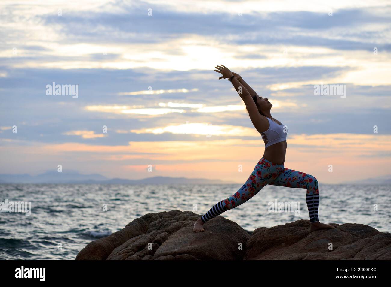 Frau, die Yoga am Meeresstrand vor dem wunderschönen, aufgehenden Himmel macht Stockfoto