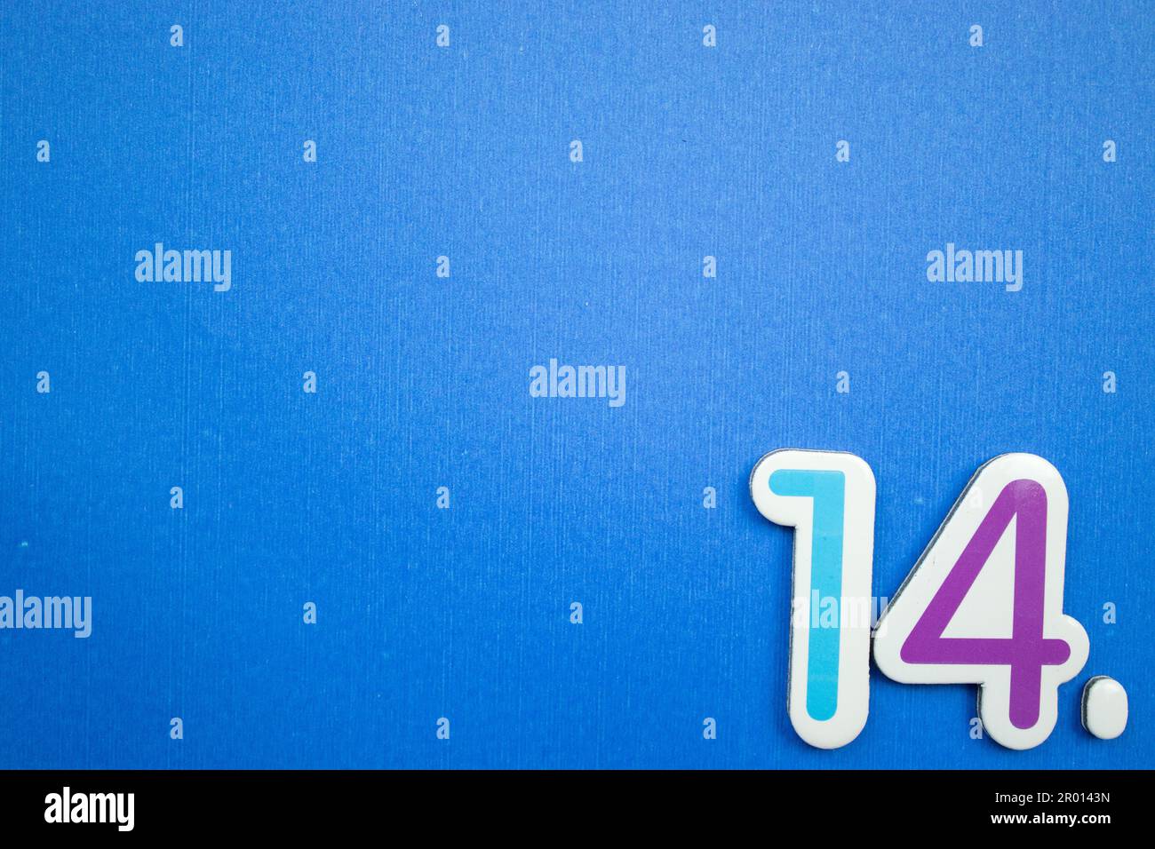 Die Nummer 14, hellblau und lila, von oben fotografiert, auf dem Rand eines blauen Hintergrunds platziert. Stockfoto
