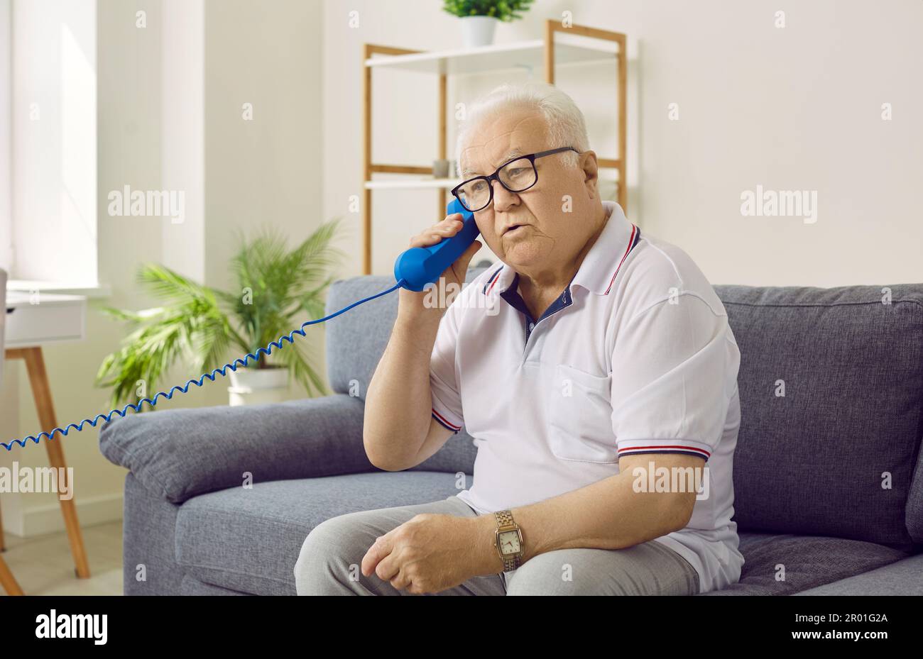 Ein Rentner redet am Telefon, während er zu Hause auf der Couch sitzt Stockfoto