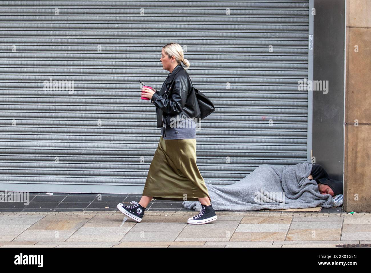 Eine Frau in einem langen grünen Rock, die an einem Obdachlosen vorbeizieht, der in Preston, Lancashire UK, vor der Tür liegt. Mai 2023. Geschäfte und Einkaufsmöglichkeiten in der High Street im Stadtzentrum von Preston am Tag der Krönung des Königs. Kredit; MediaWorldImages/AlamyLiveNews Stockfoto