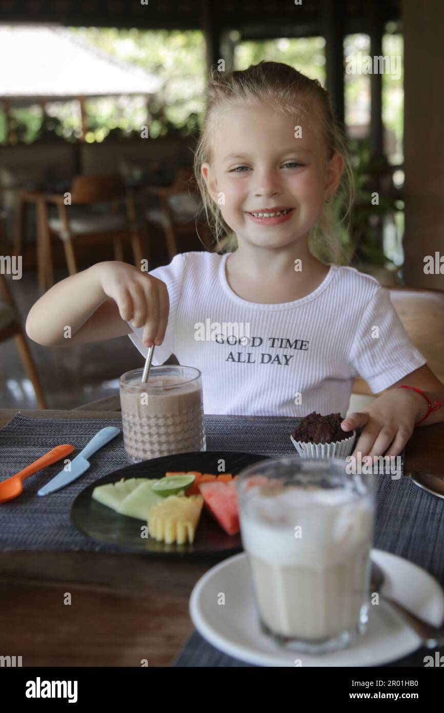 Ein süßes 5-jähriges Mädchen, das Schokoladenmilch und Obstteller im Restaurant isst Stockfoto