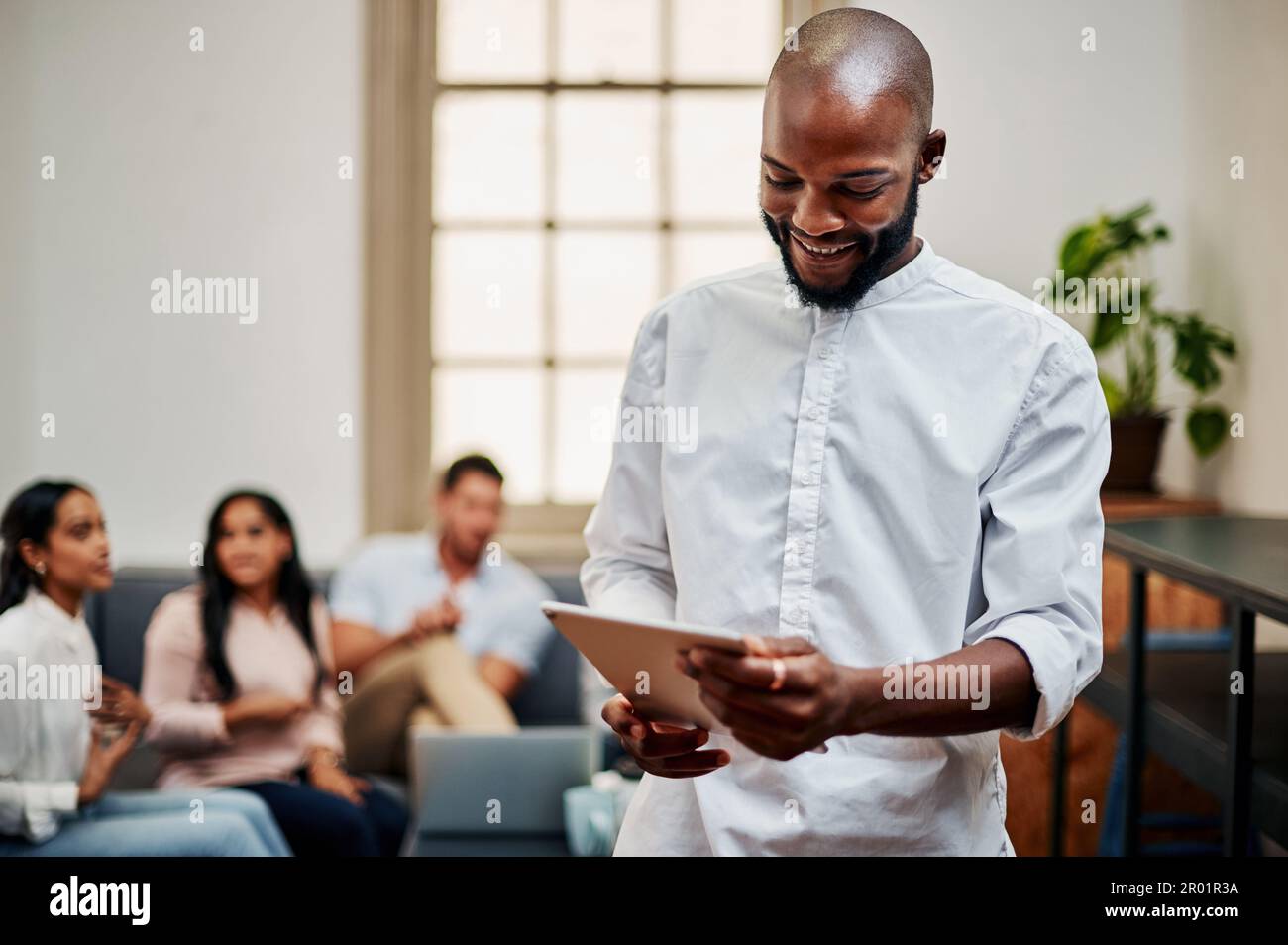 Kein Herumfummeln mehr mit Ordnern. Ein junger Geschäftsmann, der ein digitales Tablet mit seinen Kollegen im Hintergrund verwendet. Stockfoto