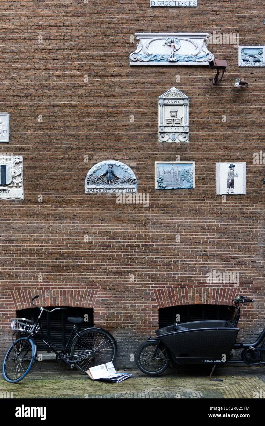Alte Giebel an einer Wand, die Handwerke und Berufe der Hausbewohner mit Fahrrädern in Amsterdam, Holland, Niederlande, zeigen. Stockfoto