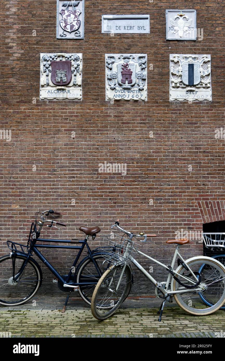 Alte Giebel an einer Wand, die Handwerke und Berufe der Hausbewohner mit Fahrrädern in Amsterdam, Holland, Niederlande, zeigen. Stockfoto