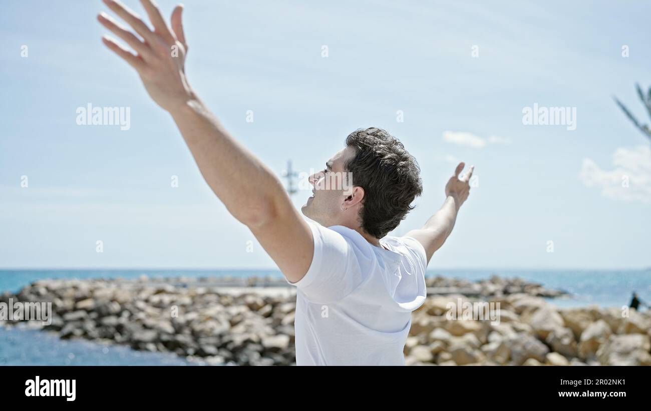 Junger lateinamerikanischer Mann atmet mit offenen Armen am Strand Stockfoto