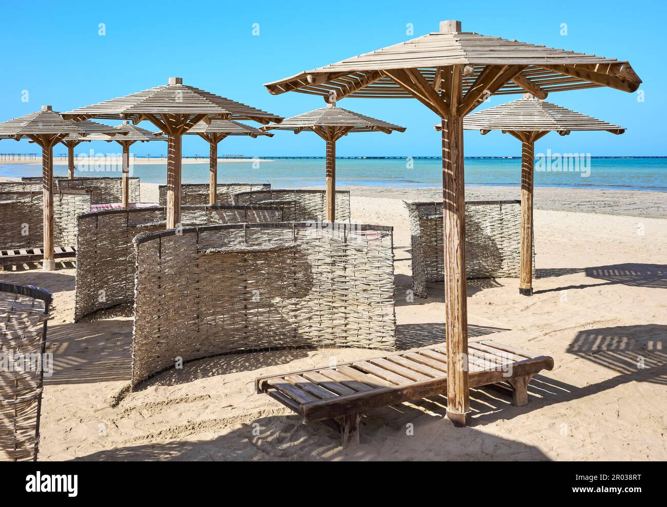 Sonnenschirme aus Holz, Sonnenliegen und Windschutzscheiben am Strand. Stockfoto