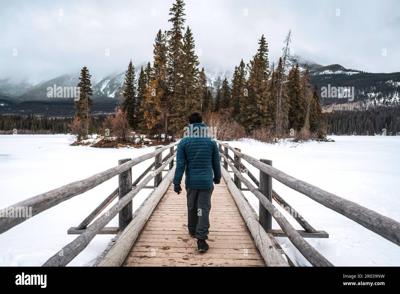 Ein Mann, der im Winter auf einer Holzbrücke zwischen dem gefrorenen See im Pyramid Lake im Jasper-Nationalpark, ab, Kanada, spaziert Stockfoto