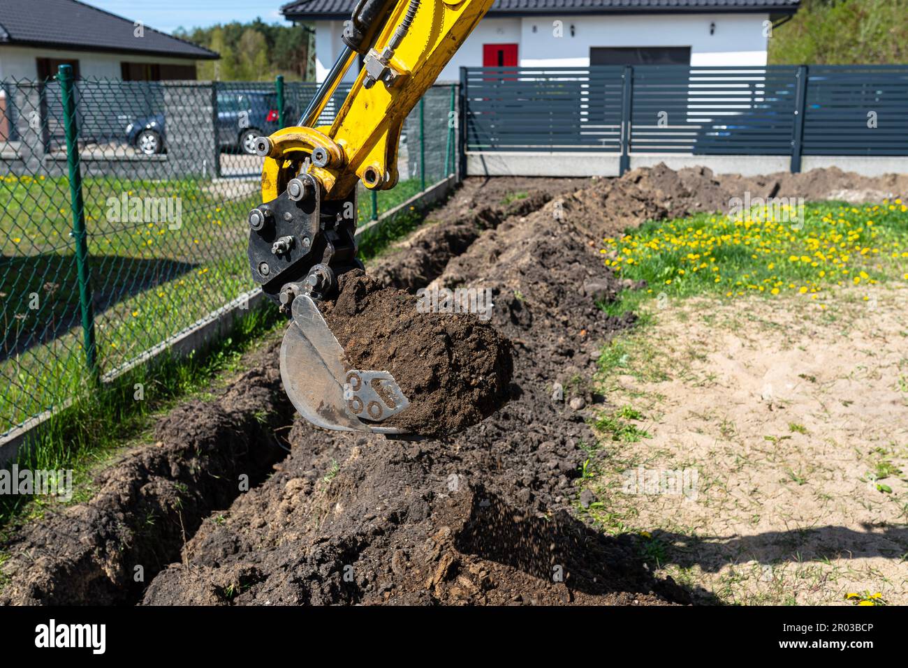 Ein Mini-Graber gräbt ein Loch im Garten entlang des Zauns zu den Abflussrohren. Stockfoto
