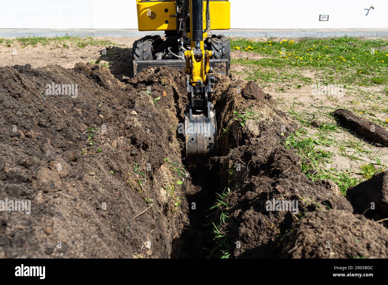 Ein Mini-Graber gräbt ein Loch im Garten entlang des Zauns zu den Abflussrohren. Stockfoto