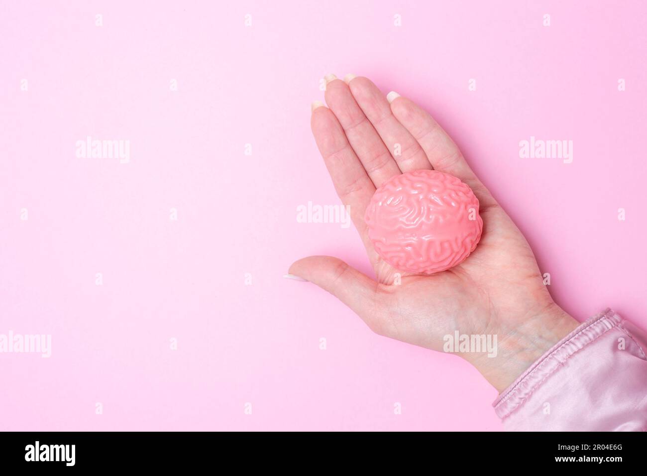 Hand hält rosa Gehirn isoliert auf rosa Hintergrund Stockfoto