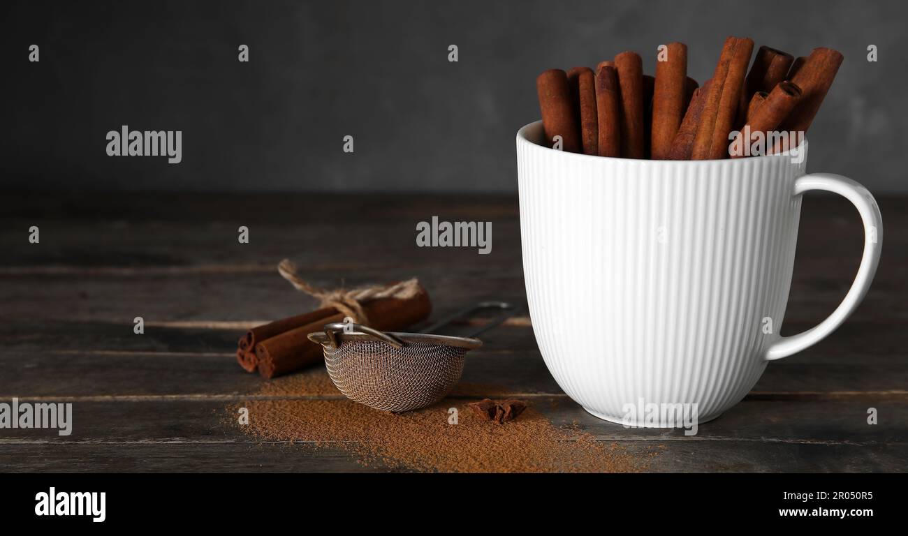 Tasse mit natürlichen Zimtstäbchen auf einem dunklen Tisch Stockfoto