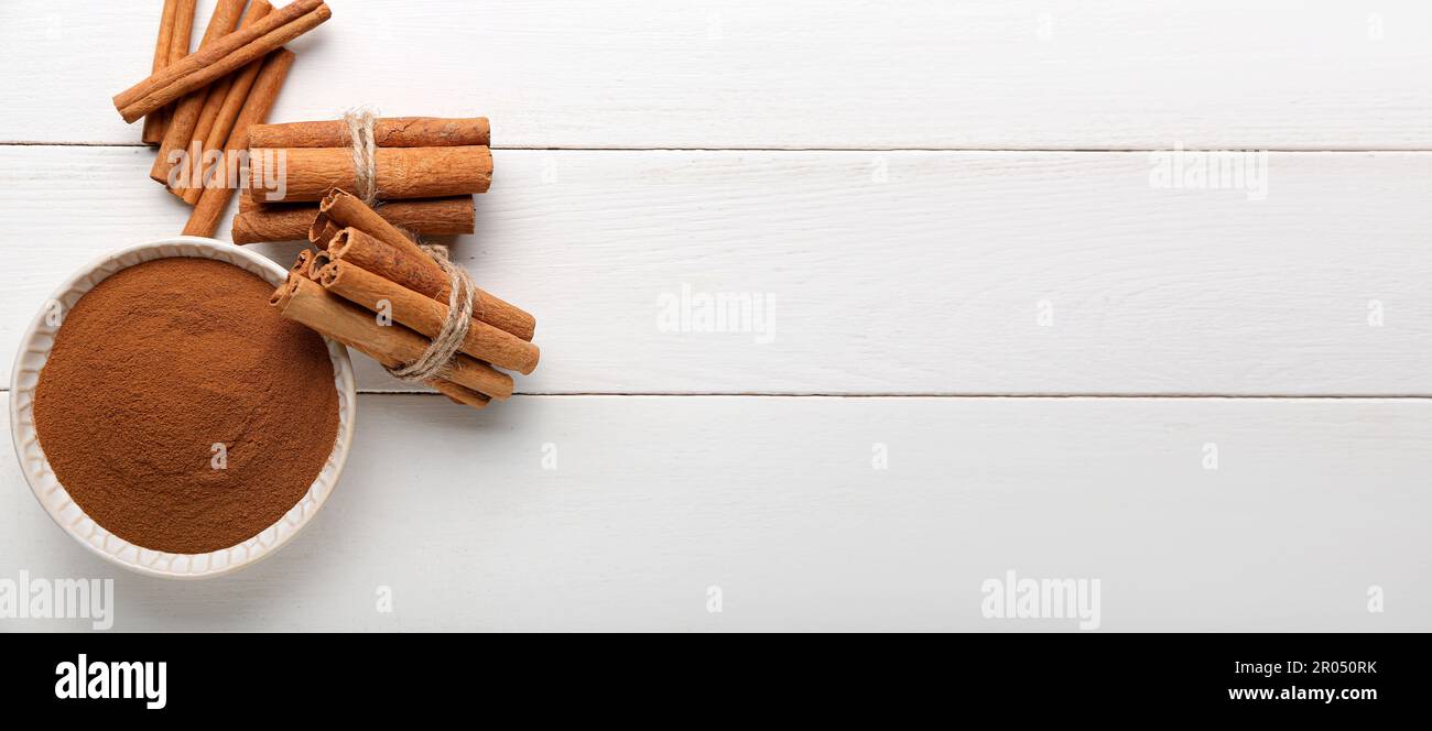 Schüssel mit Zimtpulver und Stäbchen auf weißem Holztisch. Banner für Design Stockfoto