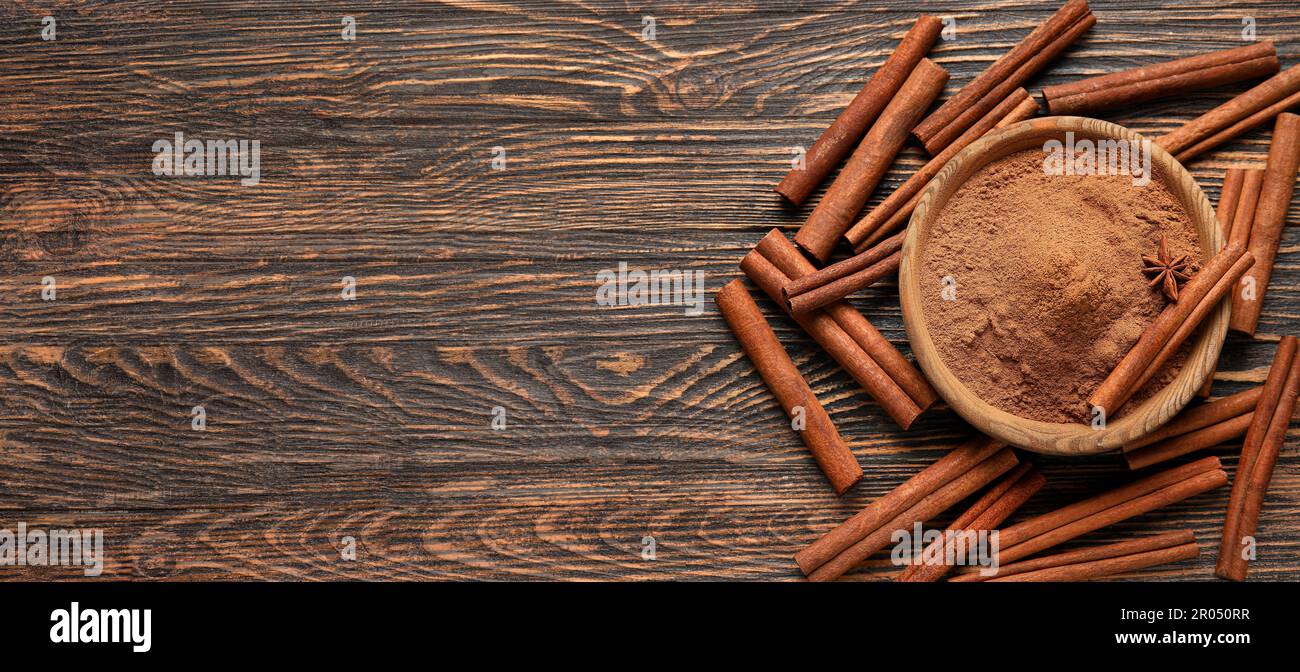 Schüssel mit natürlichem Zimtpulver und Stäbchen auf Holzhintergrund mit Platz für Text, Draufsicht Stockfoto