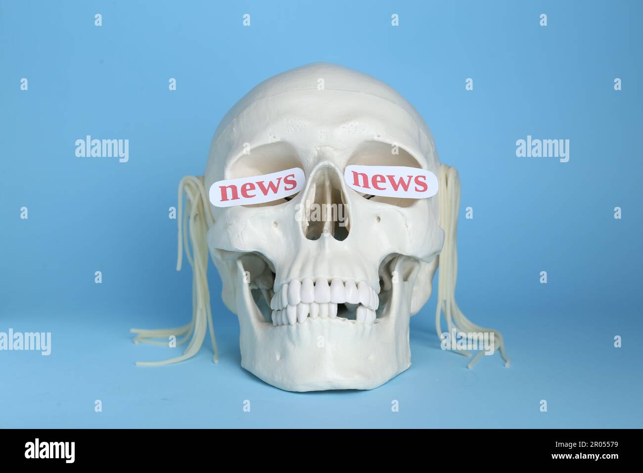 Konzept der Informations- und Medienkriegsführung. Menschlicher Schädel mit Nudeln und Wörtern Nachrichten in Augenhöhlen auf hellblauem Hintergrund Stockfoto