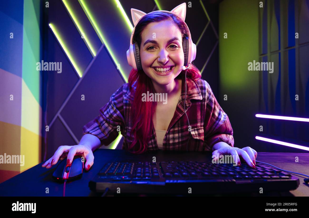 Porträt einer Gamer-Frau, die mit einem großen Lächeln in die Kamera schaut und ein aufregendes Videospiel auf ihrem Computer spielt. Glückliche junge Frau, die Navigati genießt Stockfoto