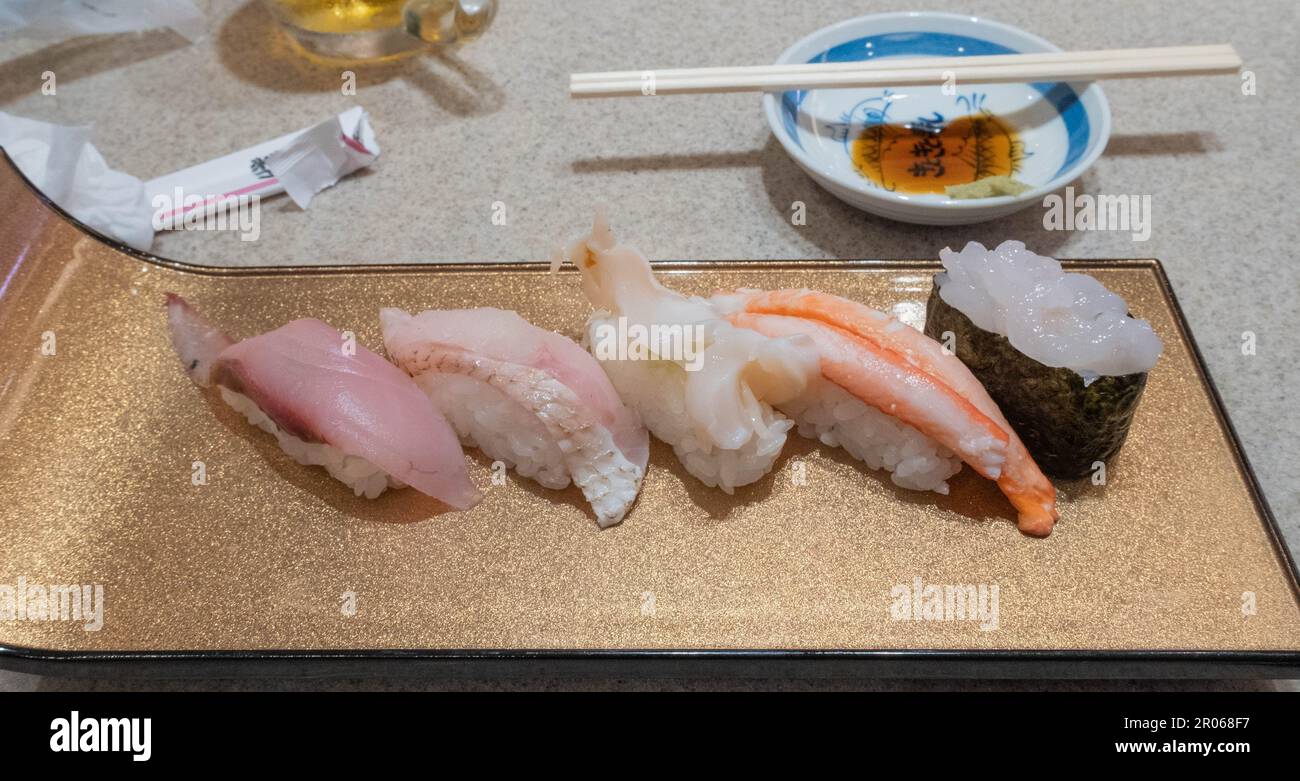 Sushi mit Thunfisch und Garnelen auf einer Goldplatte mit Essstäbchen in einem Kaitenzushi- oder Bandförderer-Sushi-Restaurant in der Toyama Station. Stockfoto
