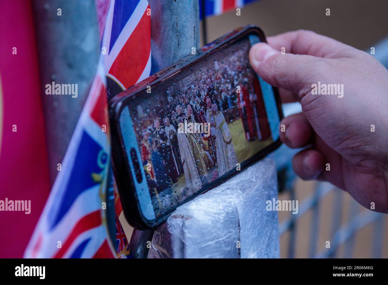 The Mall, London, Großbritannien. 6. Mai 2023 Königliche Fans in der Mall, die die Fernsehsendung der Krönung von König Karl III. Mit einem Handy im Regen sehen. Foto: Amanda Rose/Alamy Live News Stockfoto