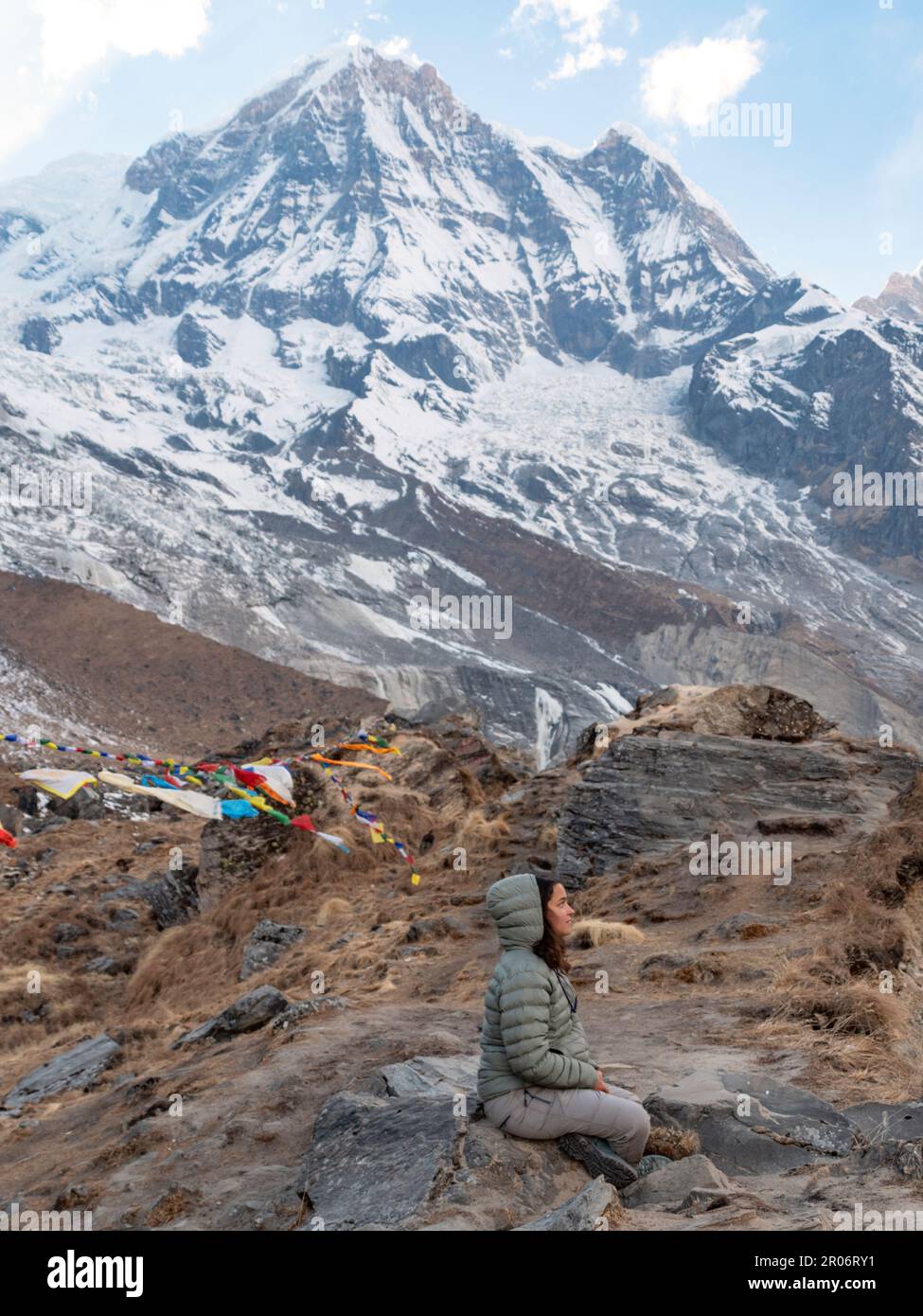 Vertikale Ansicht einer Frau, die im Annapurna Base Camp sitzt und eine Meditation durchführt, um den Geistern der Natur zu danken, nach all den Anstrengungen, die nötig waren, um dorthin zu gelangen. Stockfoto