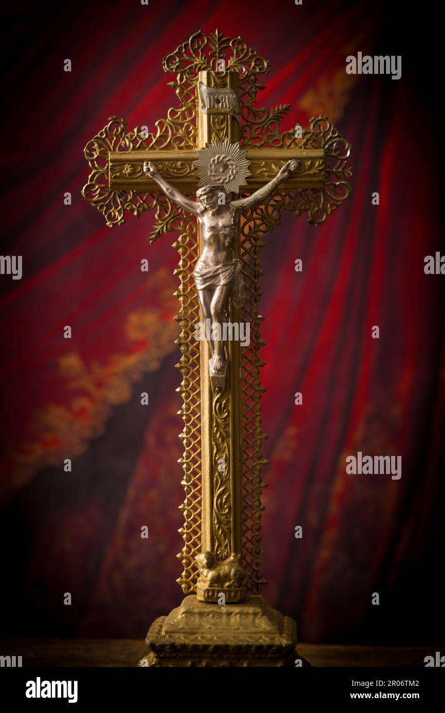 Antikes Kruzifix aus Holz und Goldfiligran, das vor einem roten Samtvorhang steht Stockfoto