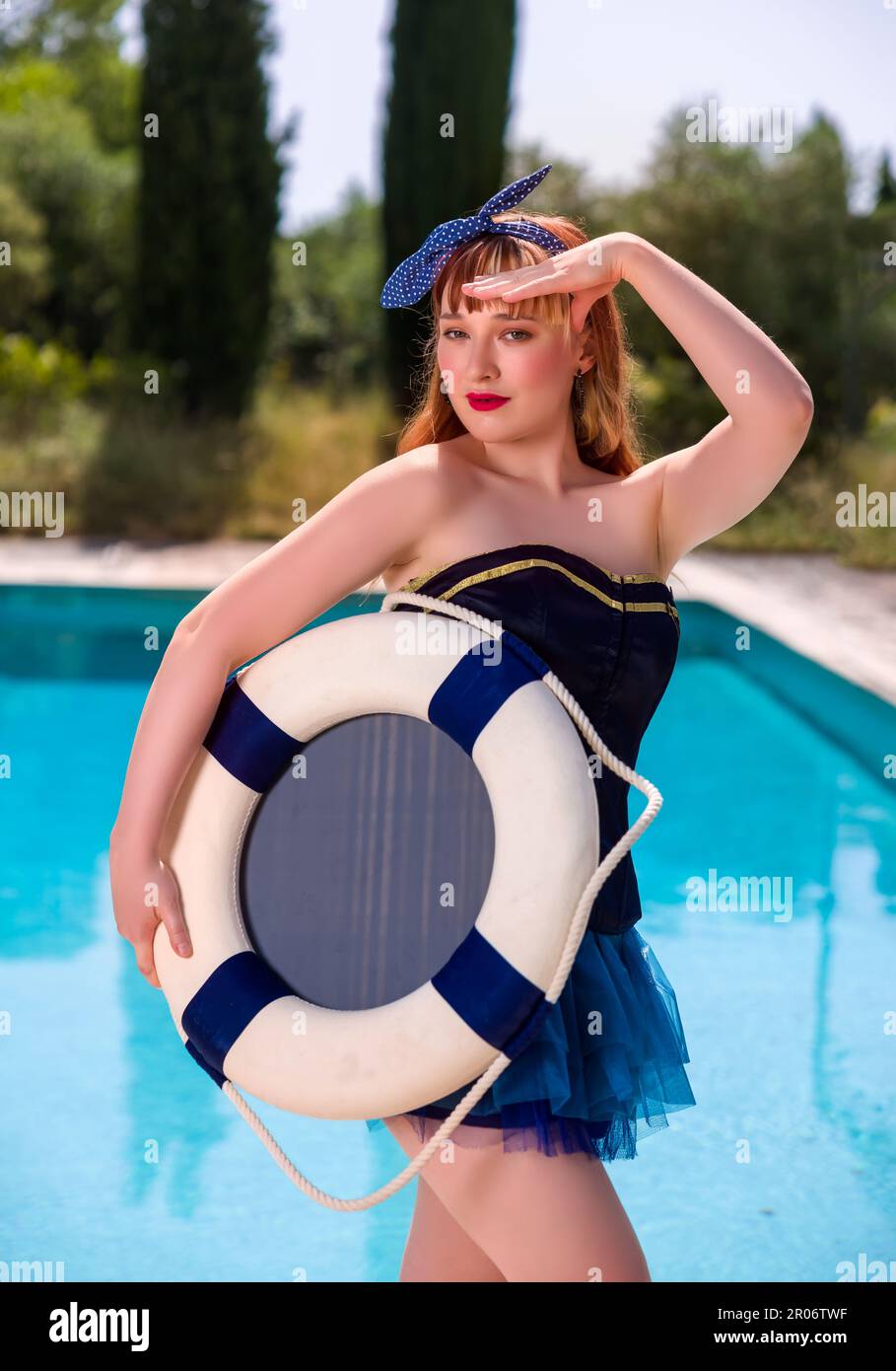 Attraktive junge Frau in einem sexy Matrosenkostüm als Pinup-Mädchen am Rande eines Schwimmbades Stockfoto