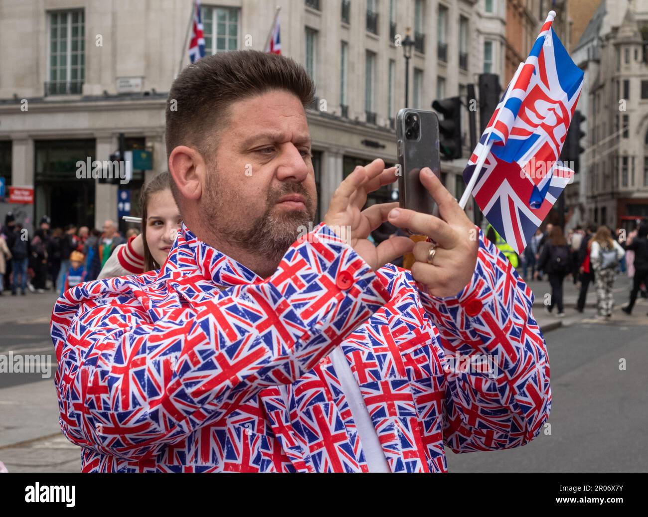 Ein überschwänglicher Mann in einem Anzug mit Gewerkschaftsflaggen, der britischen Flagge, macht ein Foto in London während der Krönung von König Karl III Seine Stockfoto