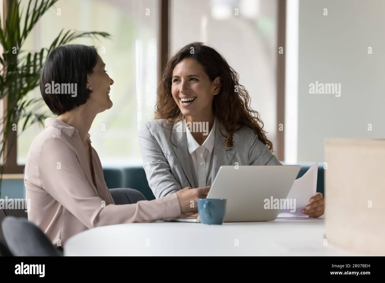 Zwei Geschäftsfrauen, die im Büro arbeiten, lachen, scherzen während des Arbeitsablaufs Stockfoto