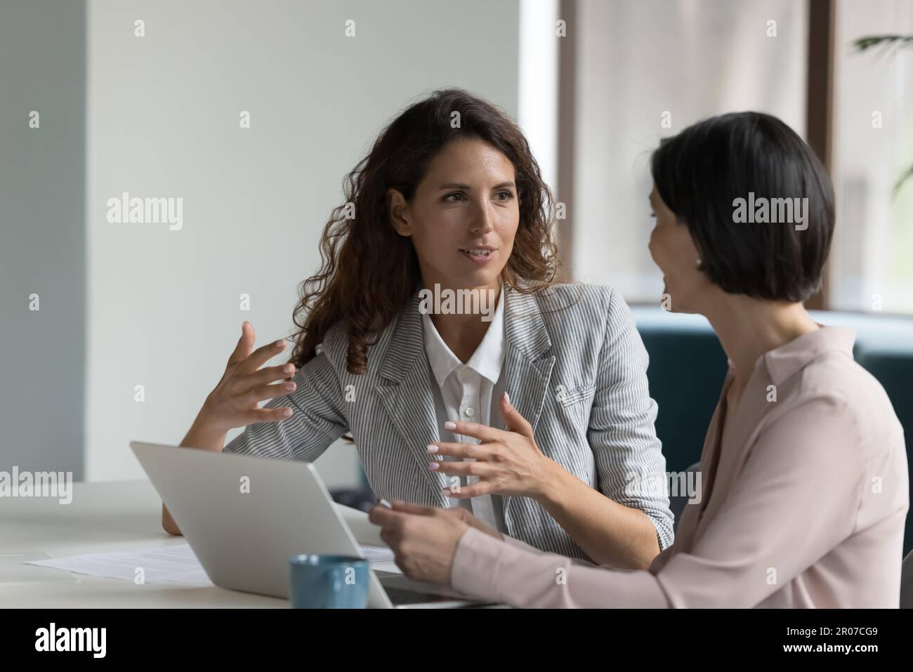 Zwei attraktive Geschäftsfrauen sitzen am Schreibtisch und besprechen Projektdetails Stockfoto