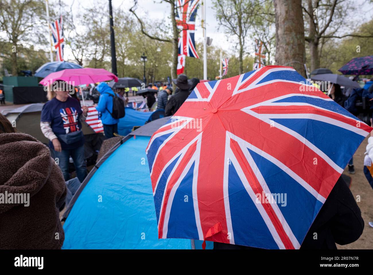 Menschen, Royalisten und königliche Fans verstecken sich unter Regenschirmen, während sintflutartige Regenfälle eintreffen, während sich die Menschen in der Mall versammeln, um sich auf die Krönung von König Karl III. Am 5. Mai 2023 in London, Großbritannien, vorzubereiten. Viele sind bereit, über Nacht zu zelten und tragen zur Feier rot-weiß und blau die Flagge der Union, bevor König Karl III. Zum König von England gekrönt wird. Stockfoto