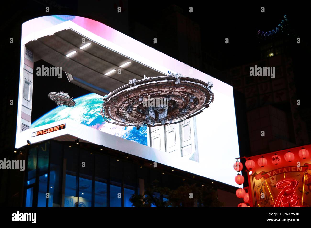 Computer graphics 3D image of a UFO (unidentified flying object) is projected on a curved surface screen in front of Shinjuku Station east entrance at Cross Shinjuku Vision in Shinjuku Ward, Tokyo on April 23, 2023. The image of the UFO has been projected on 4K resolution screen 8.16m x 18.96m on the 4th floor of the Cross Shinjuku Building.( The Yomiuri Shimbun via AP Images ) Stockfoto