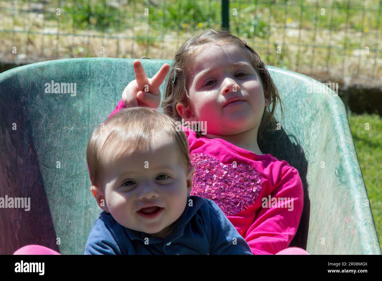 Bild von zwei niedlichen, lächelnden Kindern, die sich in einer Schubkarre halten. Brüderliche Liebe, während sie im Garten mit ihrer Schwester spielen Stockfoto